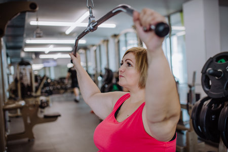 Mid adult plus size woman working out on a lat pulldown machine indoors in gymの写真素材