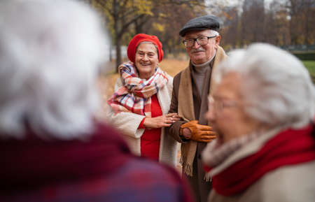 Group of happy senior friends on walk outdoors in town park in autumn, talking and laughing.