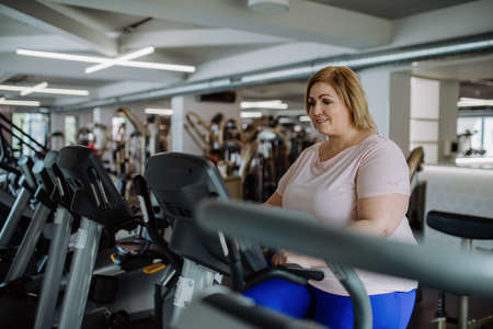 Happy mid adult overweight woman exercising on stepper indoors in gymの写真素材