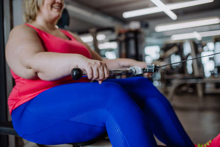 Unrecognizable plus size woman training on rowing machine machine indoors in gymの写真素材