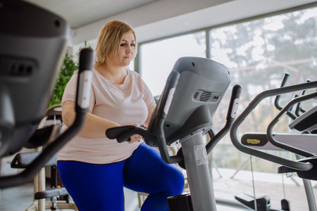 Happy mid adult overweight woman exercising on stepper indoors in gymの写真素材