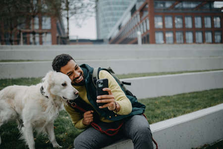 Happy young man taking selfie with his dog outdoors in town.の写真素材