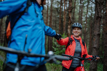 Senior couple bikers fist bumping outdoors in forest in autumn day.