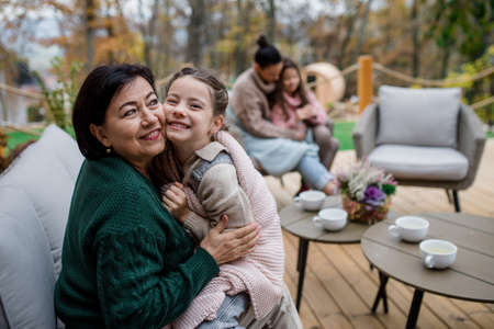 Happy little girl with grandmother sitting wrapped in blanket outdoors in patio in autumnの写真素材