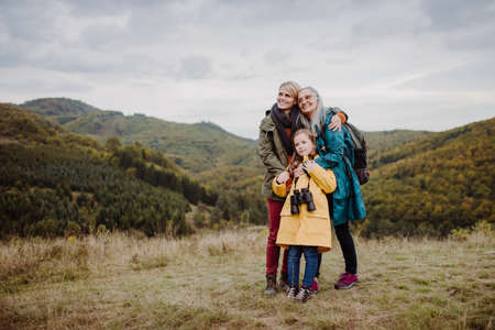 Small girl with mother and grandmother standing and lookiong at view on top of mountain.