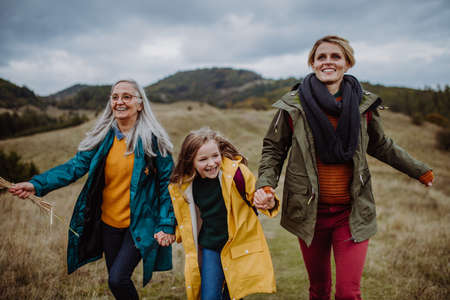 Happy small girl with mother and grandmother hiking outoors in autumn nature.の写真素材