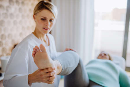 Mid adult physiotherapist woman exercising with overweight woman indoors in rehabilitation centerの写真素材