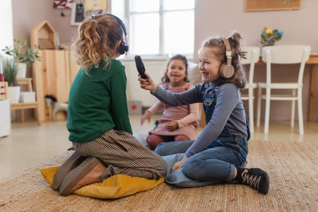 Little girls with headphones and microphone taking an interview, having fun and playing at home.の写真素材