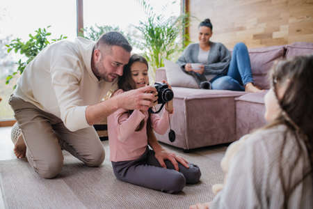 Two happy sisters with father sitting on floor and learning to use camera at homeの写真素材