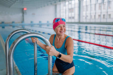 Active senior woman swimmer using ladder to get to swimming pool.の写真素材