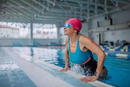 Happy senior woman getting out of the swimming pool indoors.の写真素材