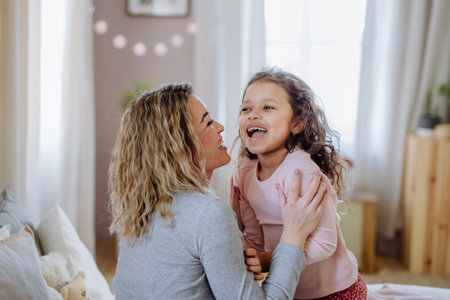 Happy mother with her little daughter hugging and having fun together on bed at home.の写真素材