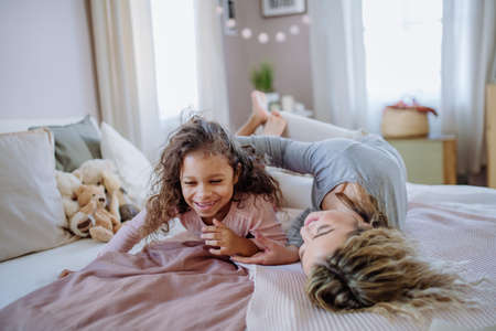 Happy mother with her little daughter hugging and having fun together on bed at home.の写真素材