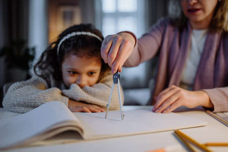 Mother helping her daughter with homework, drawing a circle with comasses in evening at home.の写真素材