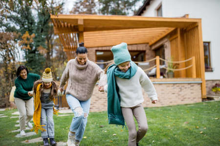 Two happy sisters with mother and grandmother holding hands and running outdoors in garden in autumn