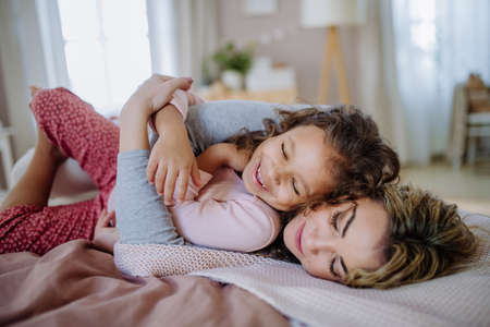 Happy mother lying on bed with her little daughter and cocoonning at home.の写真素材