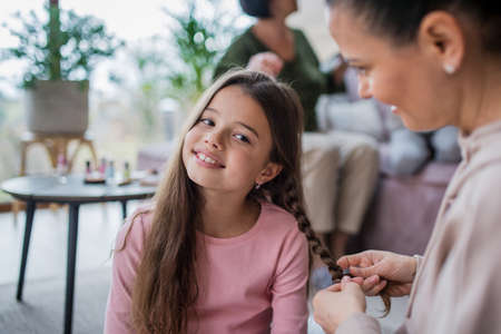 Mother making a plait to little daughter at home.の写真素材