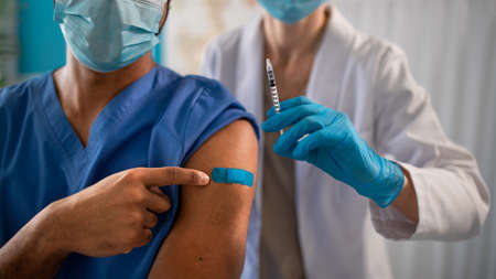 Close-up of unrecognizable doctor showing bandage on his arm after vaccince.
