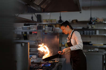 Professional chef preparing meal, flambing indoors in restaurant kitchen.の写真素材