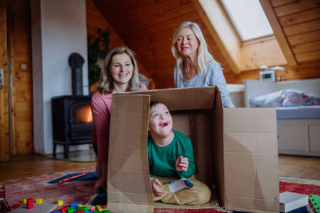 Boy with Down syndrome with his mother and grandmother playing with box together at home.の写真素材