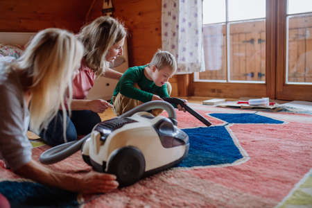 Boy with Down syndrome with his mother and grandmother vacuum cleaning at homeの写真素材