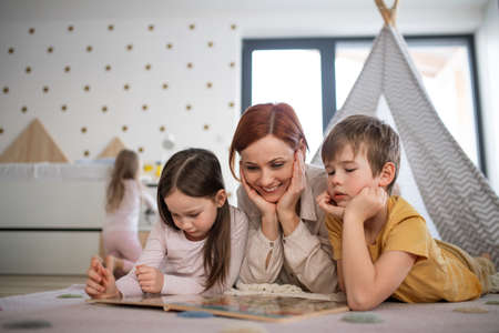 Mother with little children lying on floor and reading book at home.の写真素材