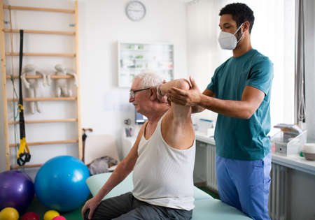 Young physiotherapist exercising with senior patient in a physic room.
