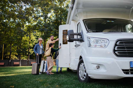 Young family with suitcases entering caravan outdoors at park.