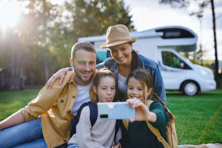 Happy young family with two children ltaking selfie with caravan at background outdoors.の写真素材