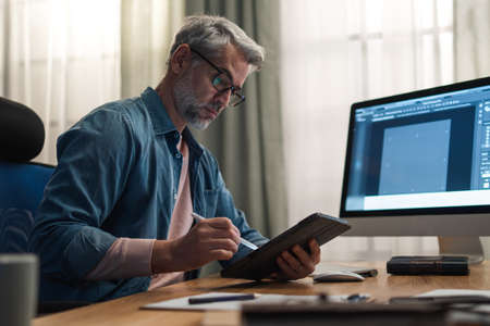 Mature man architect working on computer at desk indoors in office.の写真素材