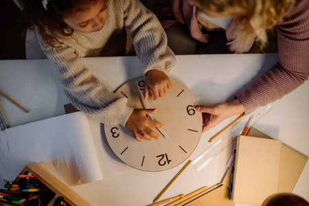 High angle view of little girl learning time with wooden clock with her mother in evening at home.の写真素材