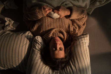 Overhead view of sad woman suffering from multiple personality disorders lying in bed.の写真素材