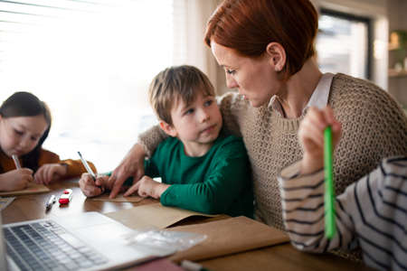Mother of three little children supervising them when diong homework at home.の写真素材