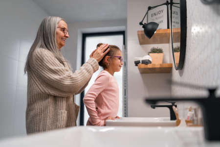 Senior grandmother and granddaughter standing indoors in bathroom, daily routine concept.の写真素材