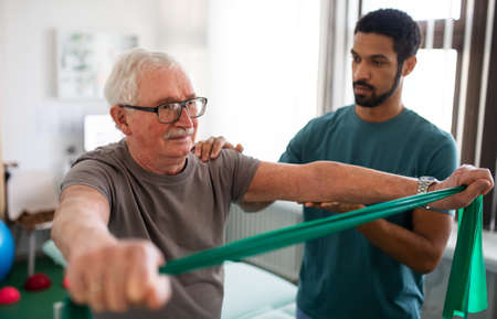 Young physiotherapist exercising with senior patient in a physic room