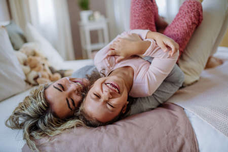 Happy mother with her little daughter hugging and having fun together on bed at home.の写真素材