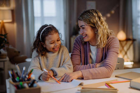 Little girl doing homework with her mother in evening at home.