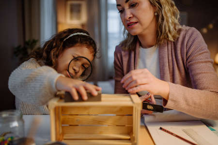 Happy little girl renovating a wooden crate together with her mother at home.