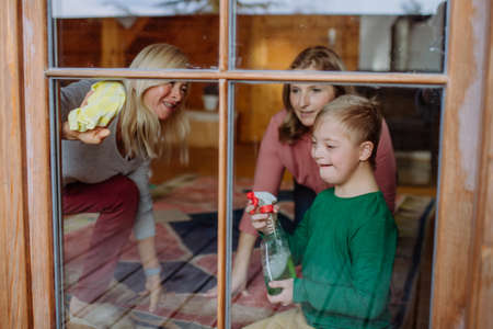 Boy with Down syndrome with his mother and grandmother cleaning window at home.の写真素材