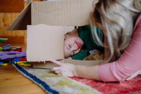 Boy with Down syndrome with his mother playing with box together at home.の写真素材