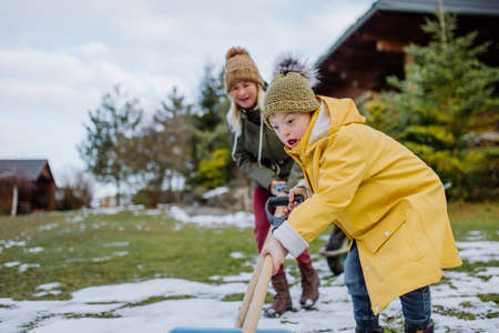 Boy with Down syndrome with his mother clearing snow from path with shovel in front of house.の写真素材