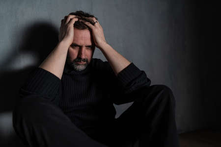 Depressed mature man, alone in darkness, mental health concept.