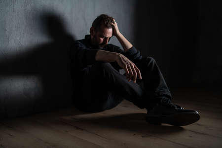 Sad mature man, alone in darkness, sitting and thinking.