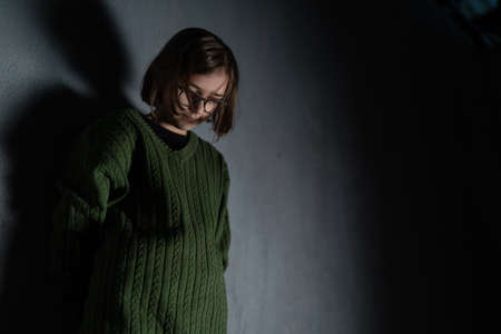 Sad little girl, alone in darkness, standing and thinking.の写真素材