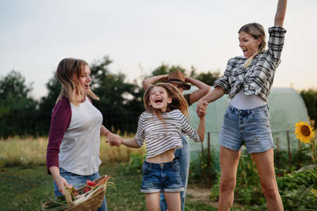 Happy little girl with mother and aunt jumping outdoors at community farm.の写真素材