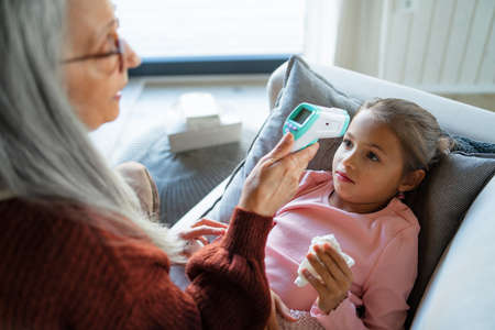 Grandmother taking care of her ill grandchild lying on sofa