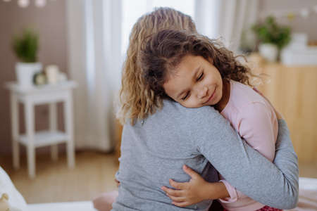 Happy mother with her little daughter hugging together on bed at home.の写真素材