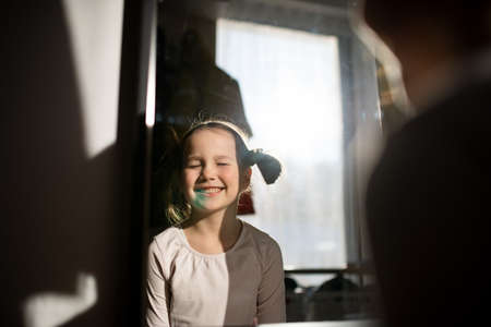 Little girl with blue stain on her face smiling with eyes closed at home.の写真素材
