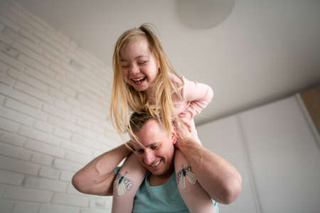 Father holding his little daughter with Down syndrome on shoulders at home.