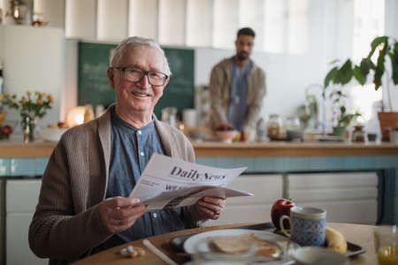 Smiling elderly man enjoying breakfast and reading newspaper in nursing home care center.の写真素材